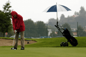 golfer playing in the rain wearing a raincoat with an umbrella protecting his clubs
